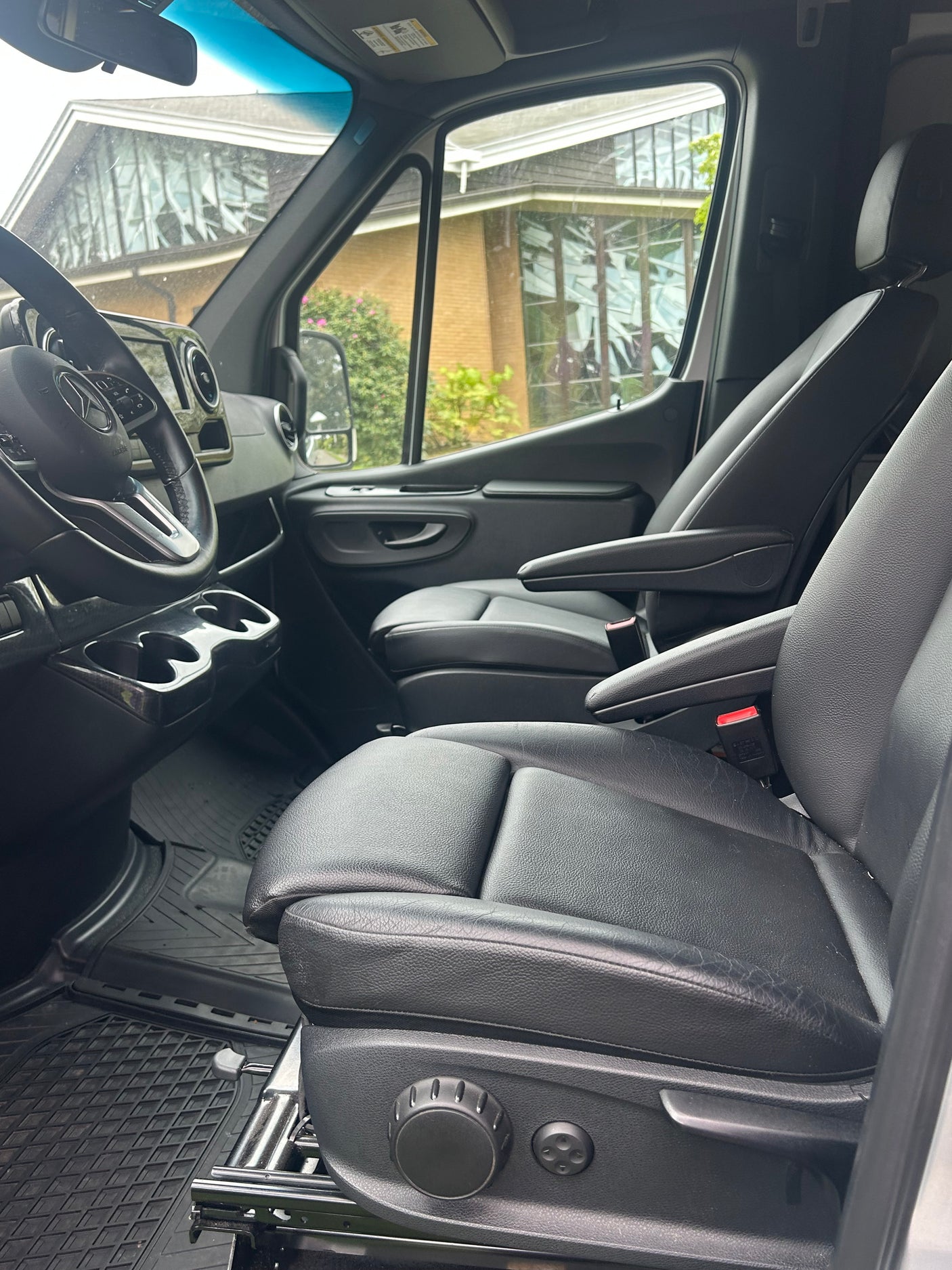 Spacious rv rental interior with black leather adjustable driver/passenger seats, steering wheel, dashboard, and cup holders.