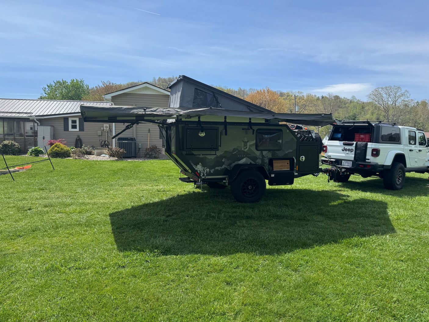 Off-road RV rental: a green overland trailer with an awning extended, hitched to a white Jeep Gladiator, ready for adventure.