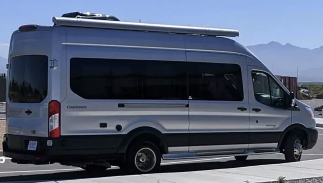 A silver Ford Transit camper van, ideal for RV rental. Equipped with an awning for your travels.