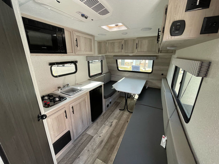 parked on gravel. Other RVs and holiday decor in background.|A 'SPORTSMEN Classic' travel trailer with awning extended in an RV rental lot