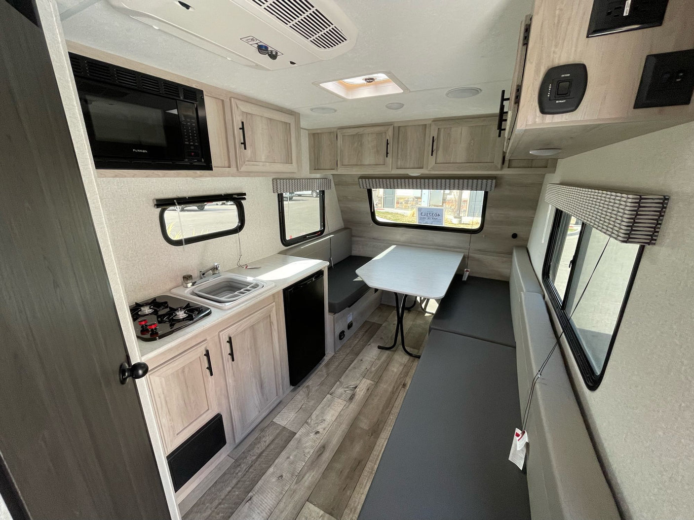 parked on gravel. Other RVs and holiday decor in background.|A 'SPORTSMEN Classic' travel trailer with awning extended in an RV rental lot