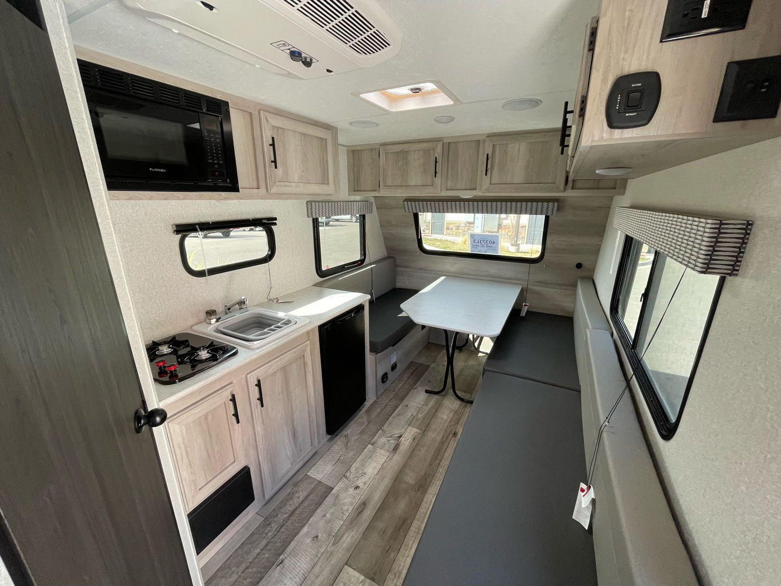 parked on gravel. Other RVs and holiday decor in background.|A 'SPORTSMEN Classic' travel trailer with awning extended in an RV rental lot
