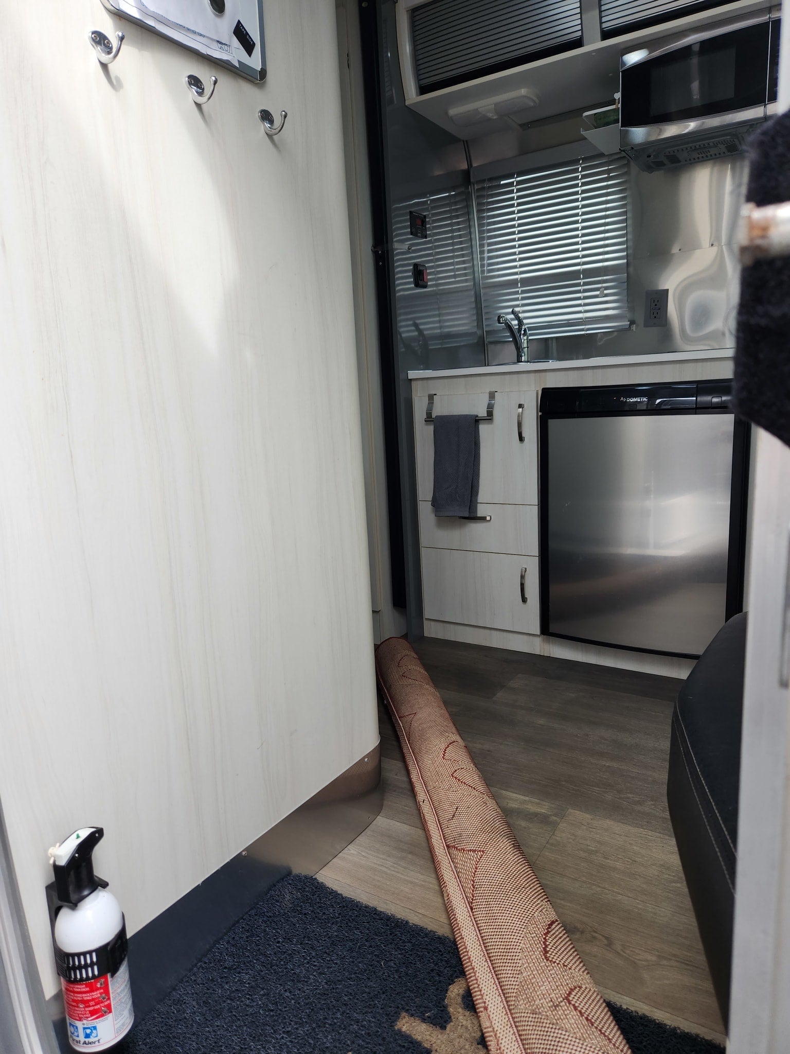 Compact RV rental interior: kitchen with Dometic fridge, microwave, sink, and a fire extinguisher by the entryway rug.