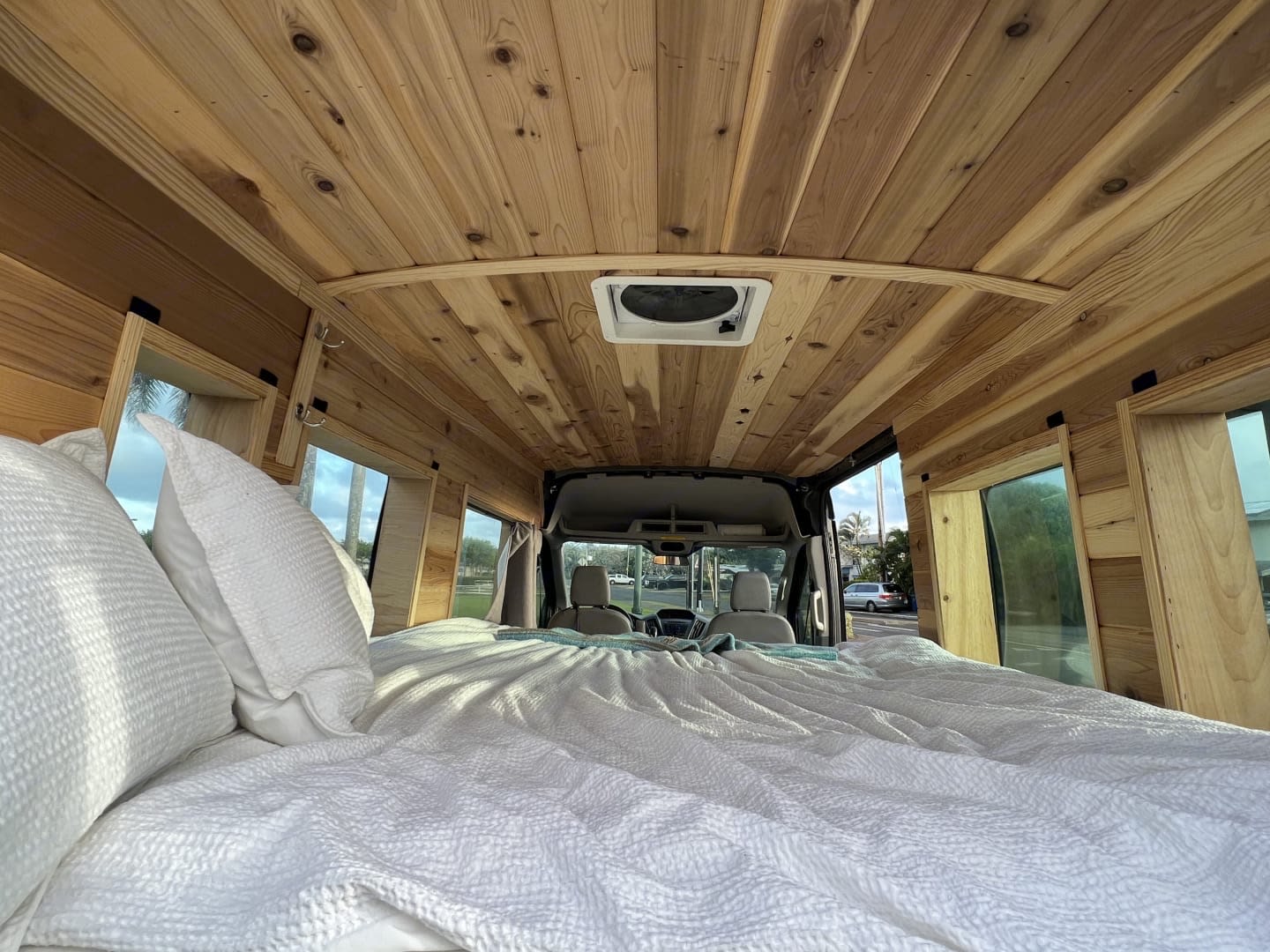 RV rental's inviting interior: A wood-paneled camper van with a large bed, cozy pillows, and window views.