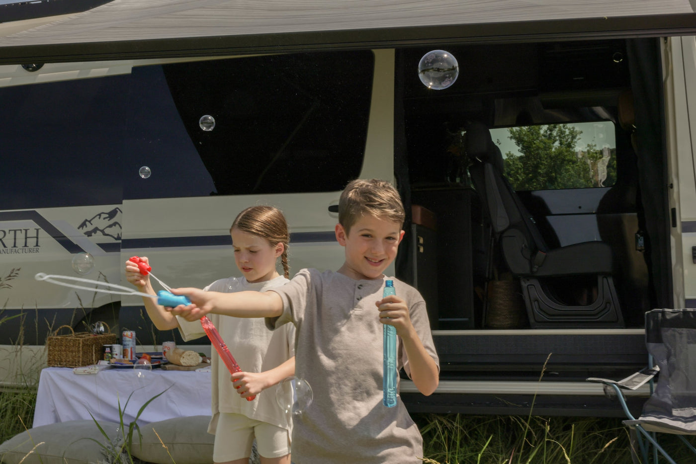 A boy and girl happily blow bubbles beside their RV rental, set up for an outdoor picnic, enjoying family time. — photo 14
