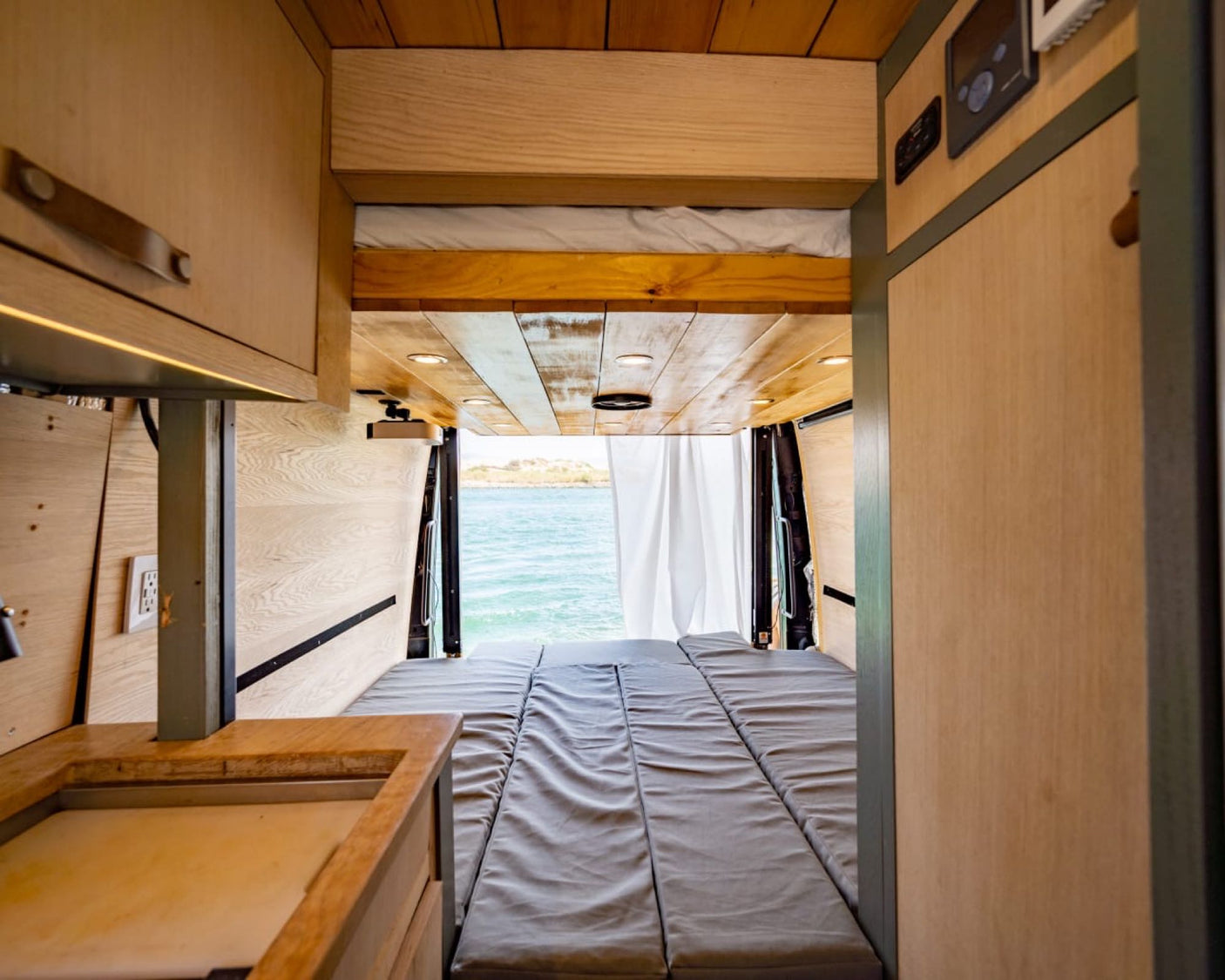 Inside a customized rv rental van: a comfy modular bed with an expansive ocean view out the back.