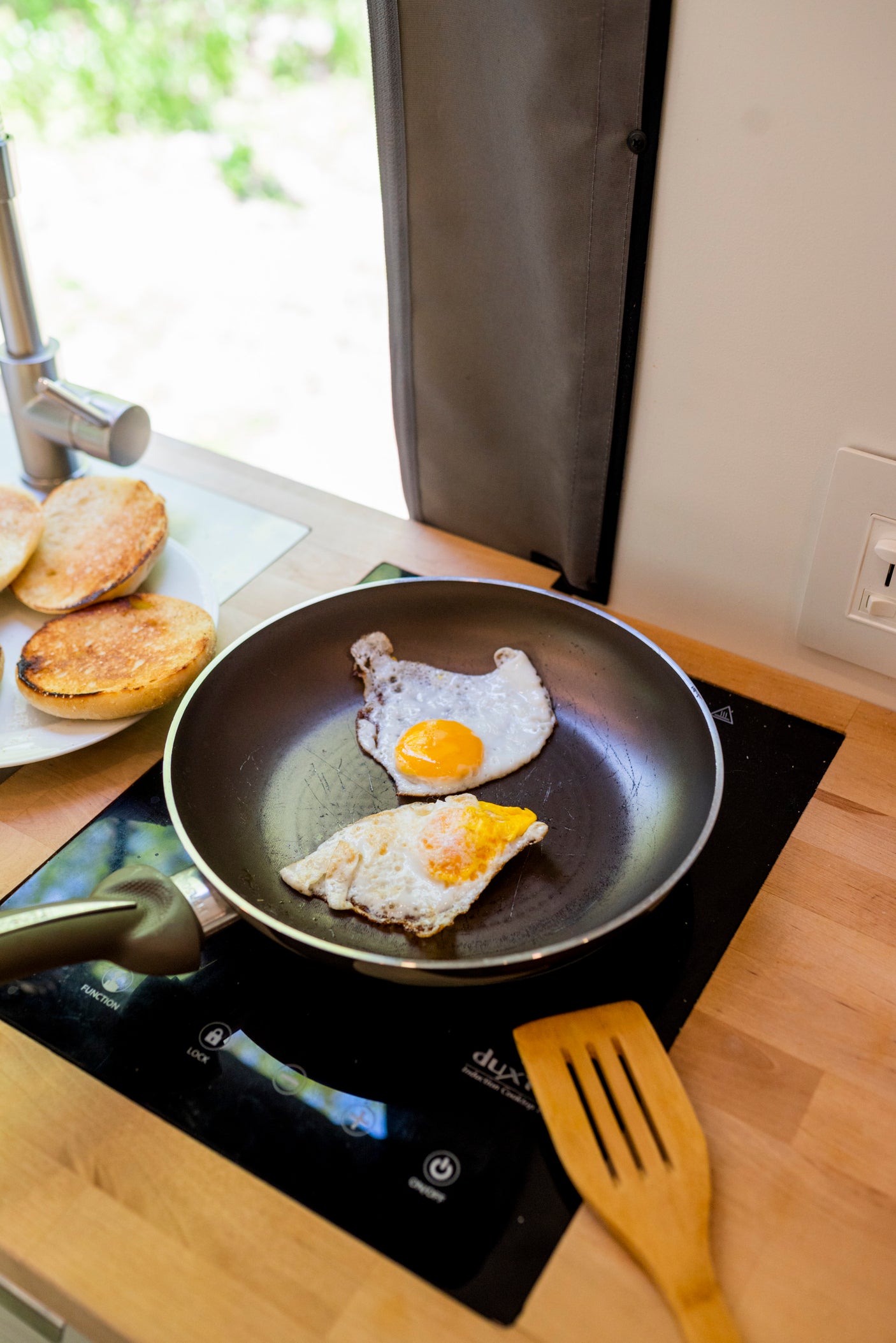 Breakfast in your RV rental! Two fried eggs sizzle on an induction cooktop, with toasted buns nearby. Perfect trip start.