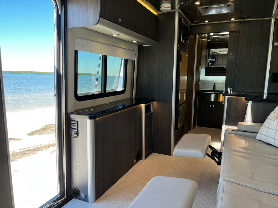 Experience premium RV rental travel with this interior, featuring an open door to a sandy beach & clear water.