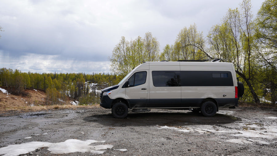 An off-road RV rental camper van on a muddy path overlooking a forest with melting snow. Ready for your nature adventure!