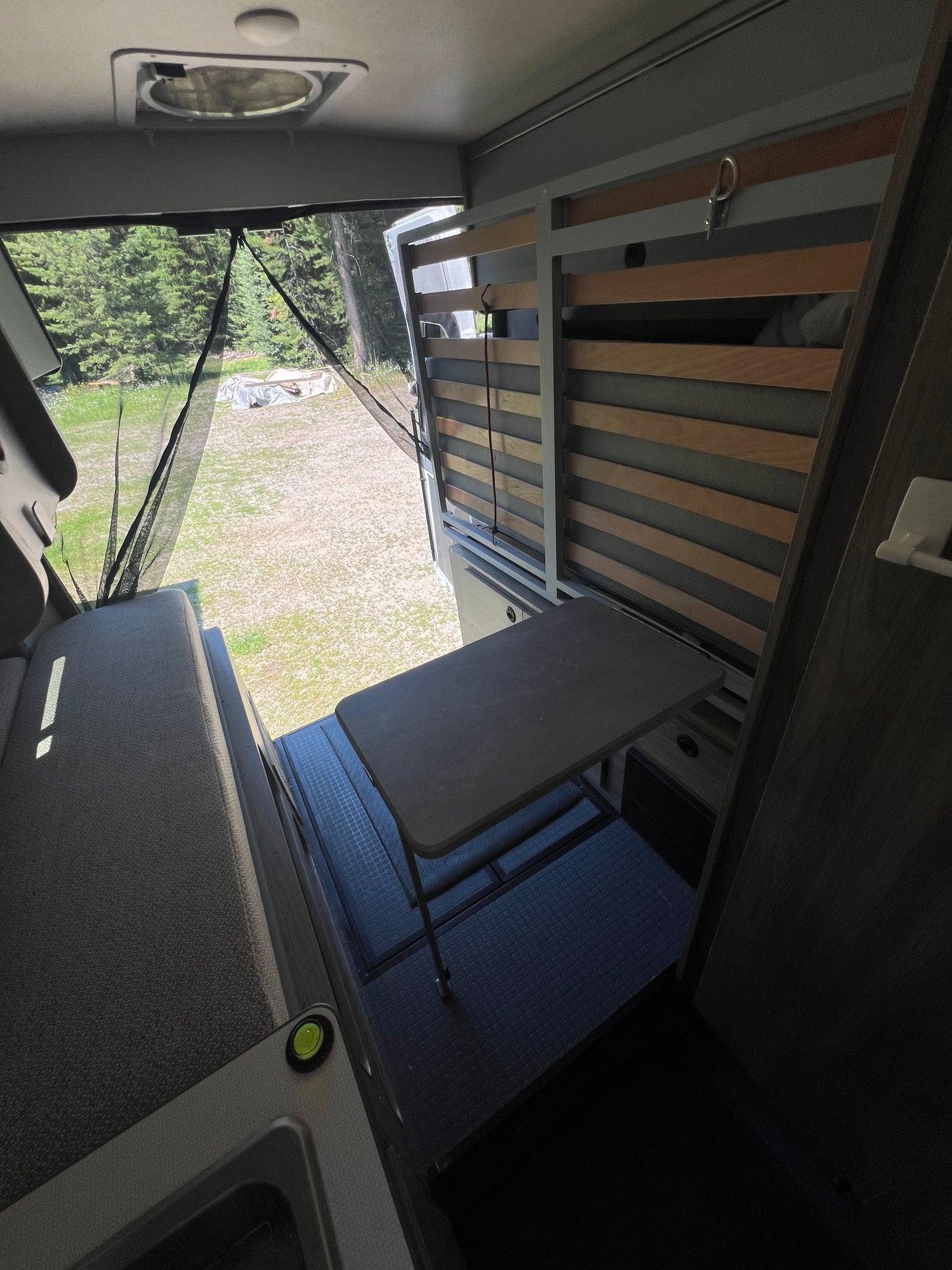 Inside an rv rental: versatile interior with a cozy bench, extendable table, and slatted bed frame looking out to nature.