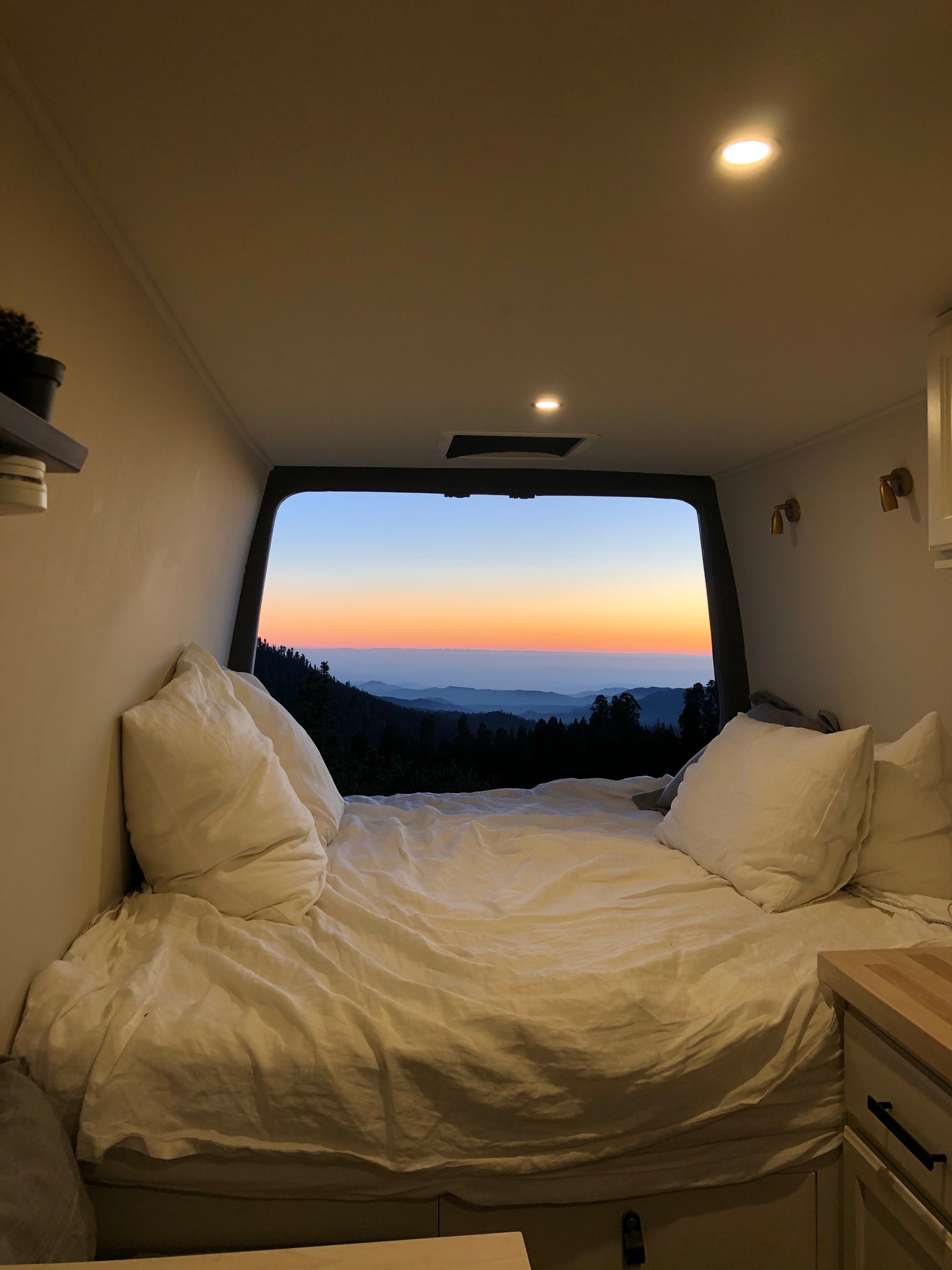 Cozy RV rental interior with a bed and stunning mountain sunset view. Perfect for van life adventures!