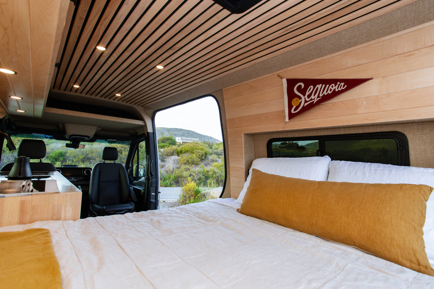 Modern rv rental interior: wood slat ceiling, comfy bed, kitchenette, and scenic nature view from the camper van.