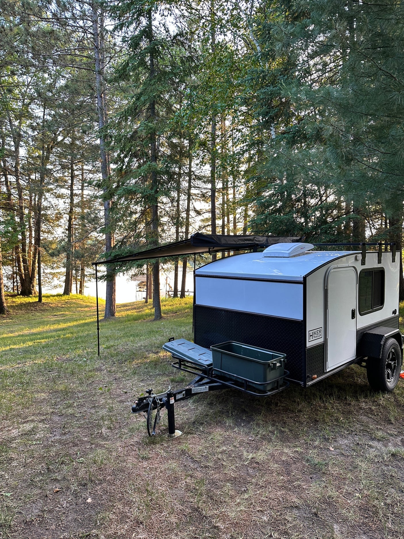 This teardrop RV rental is parked on grass by a sparkling lake