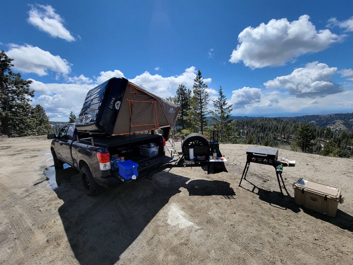 Truck with rooftop tent, grill, & cooler set up for camping in scenic mountains. An ideal RV rental alternative for adventure.