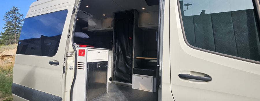 Inside an RV rental van: custom interior with compact kitchen, fridge, storage, and sleeping area.