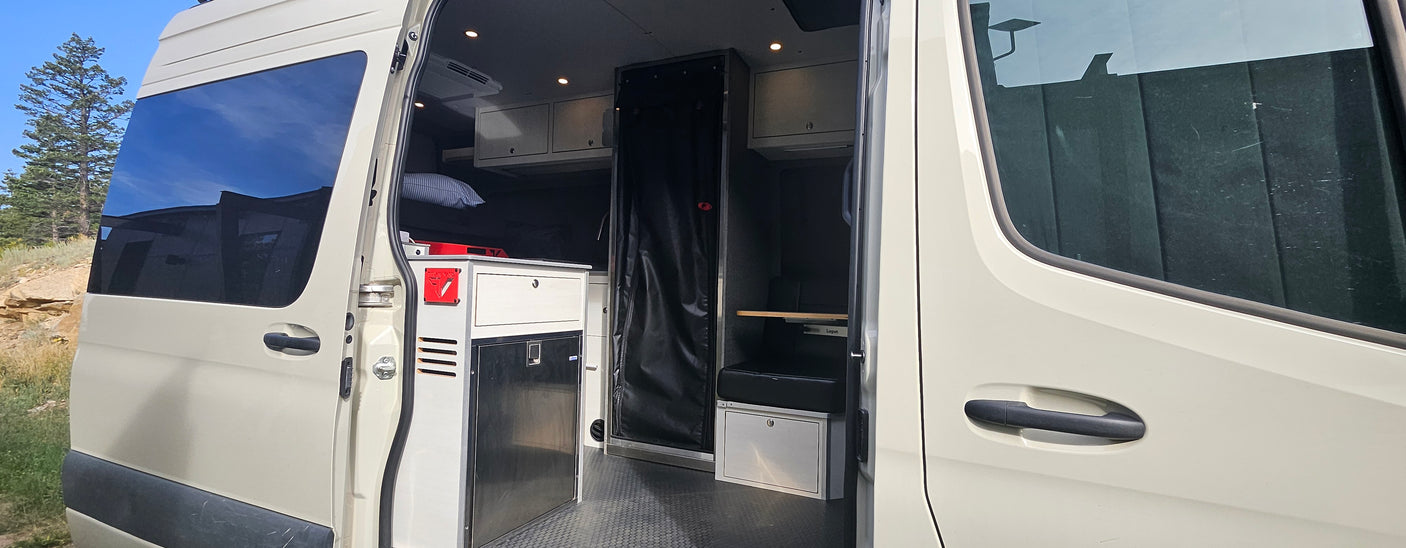 Inside an RV rental van: custom interior with compact kitchen, fridge, storage, and sleeping area.