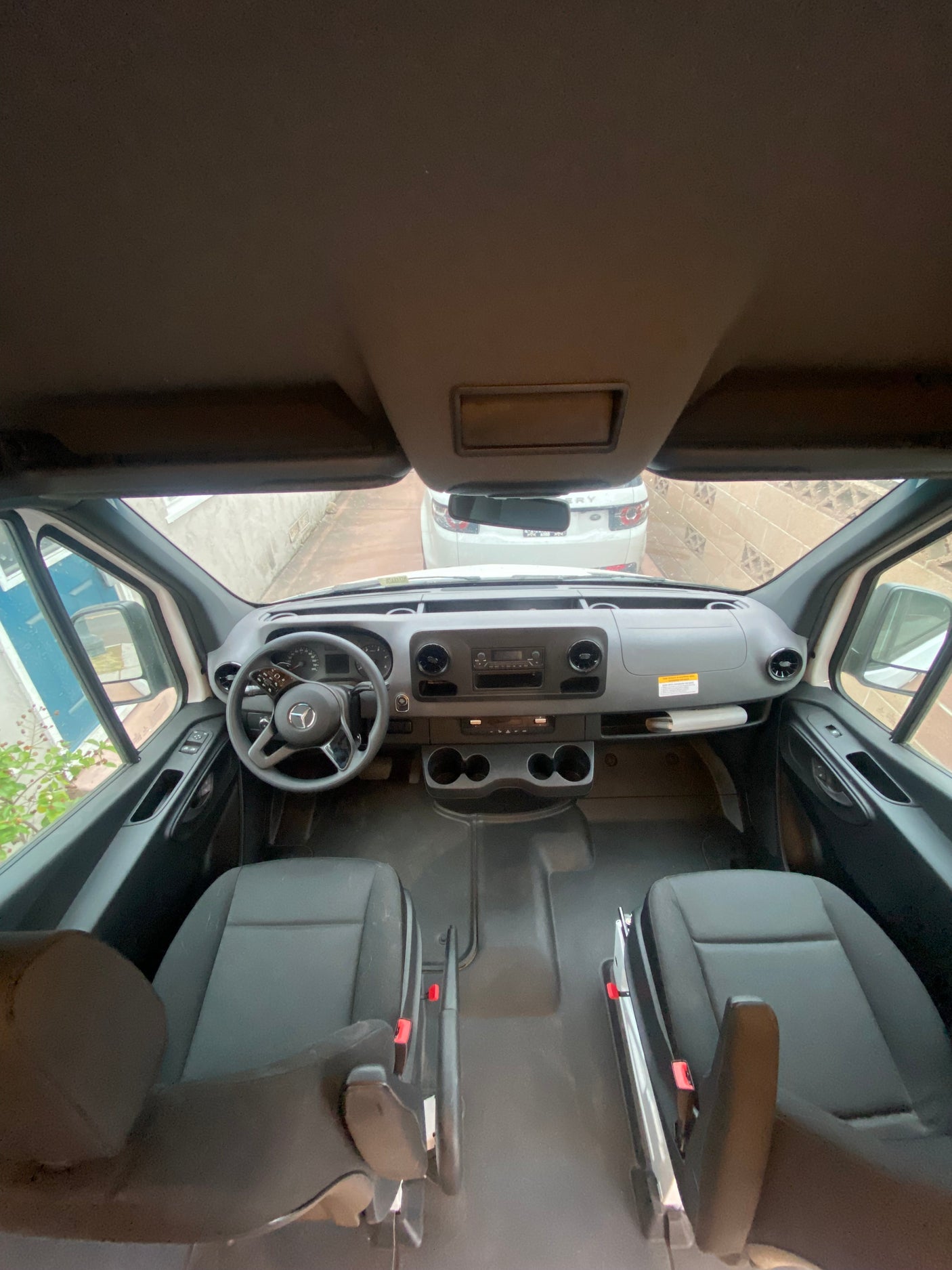 An RV rental's spacious front cabin shows the dashboard, steering wheel, and front seats, with a view of a white SUV outside.