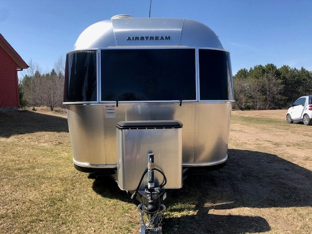Front view of an Airstream rv rental: a shiny silver travel trailer parked on a grassy field with a red building nearby.