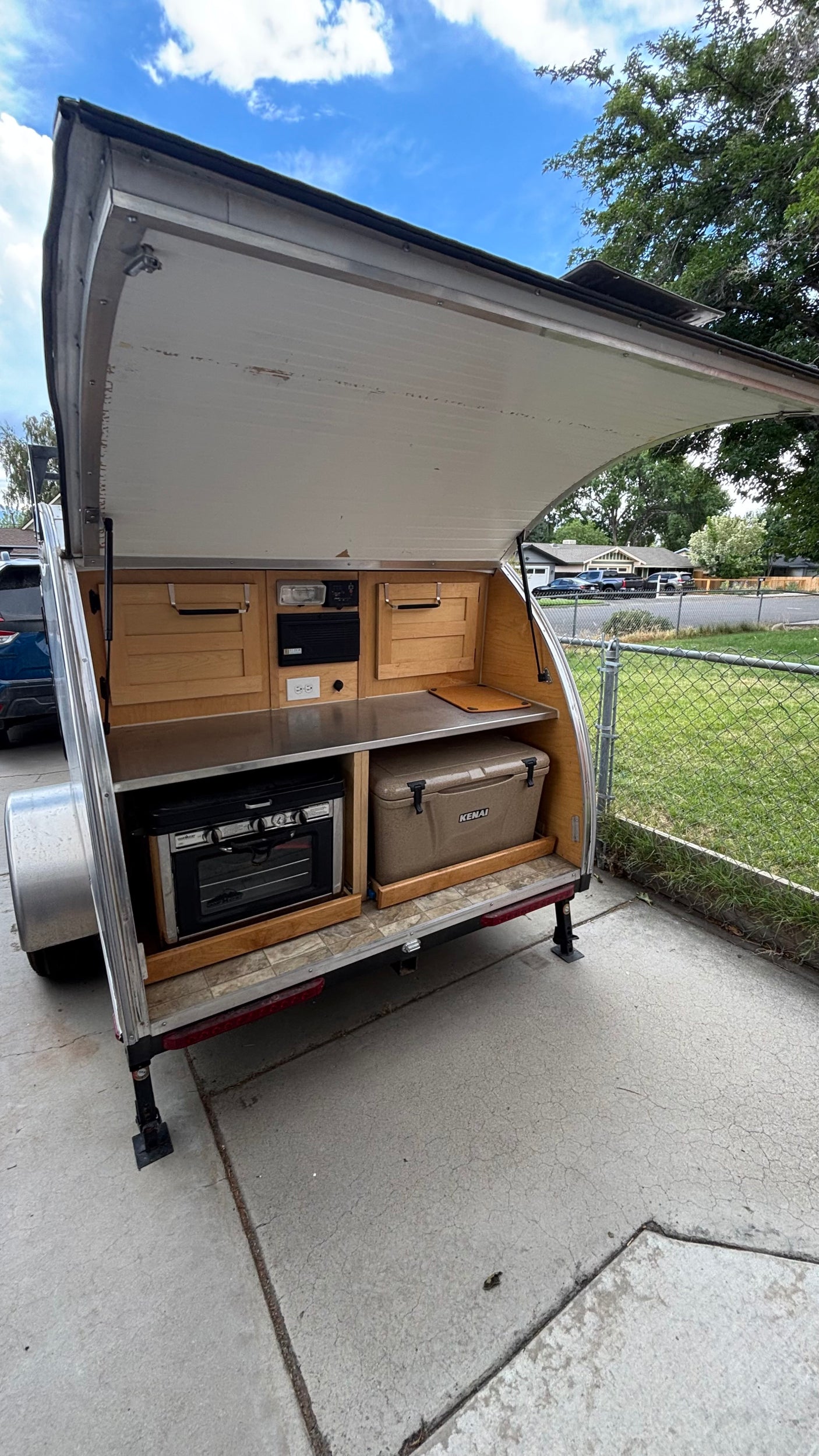 Explore this compact teardrop camper rv rental's outdoor kitchen, featuring a stove, cooler, and countertop for adventures.