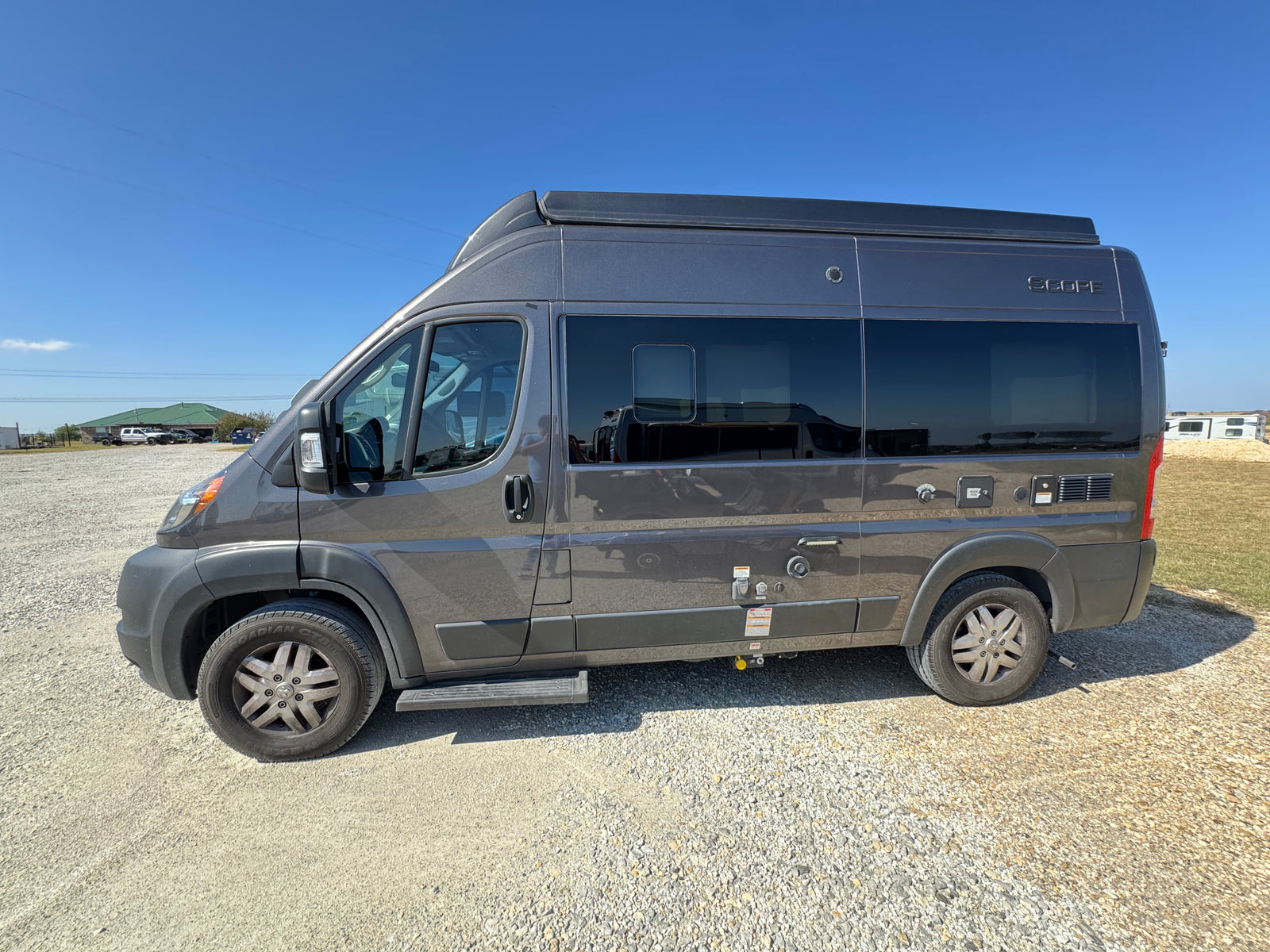 Grey Scope camper van, an RV rental, parked on gravel under a clear blue sky. Ready for your next road trip.