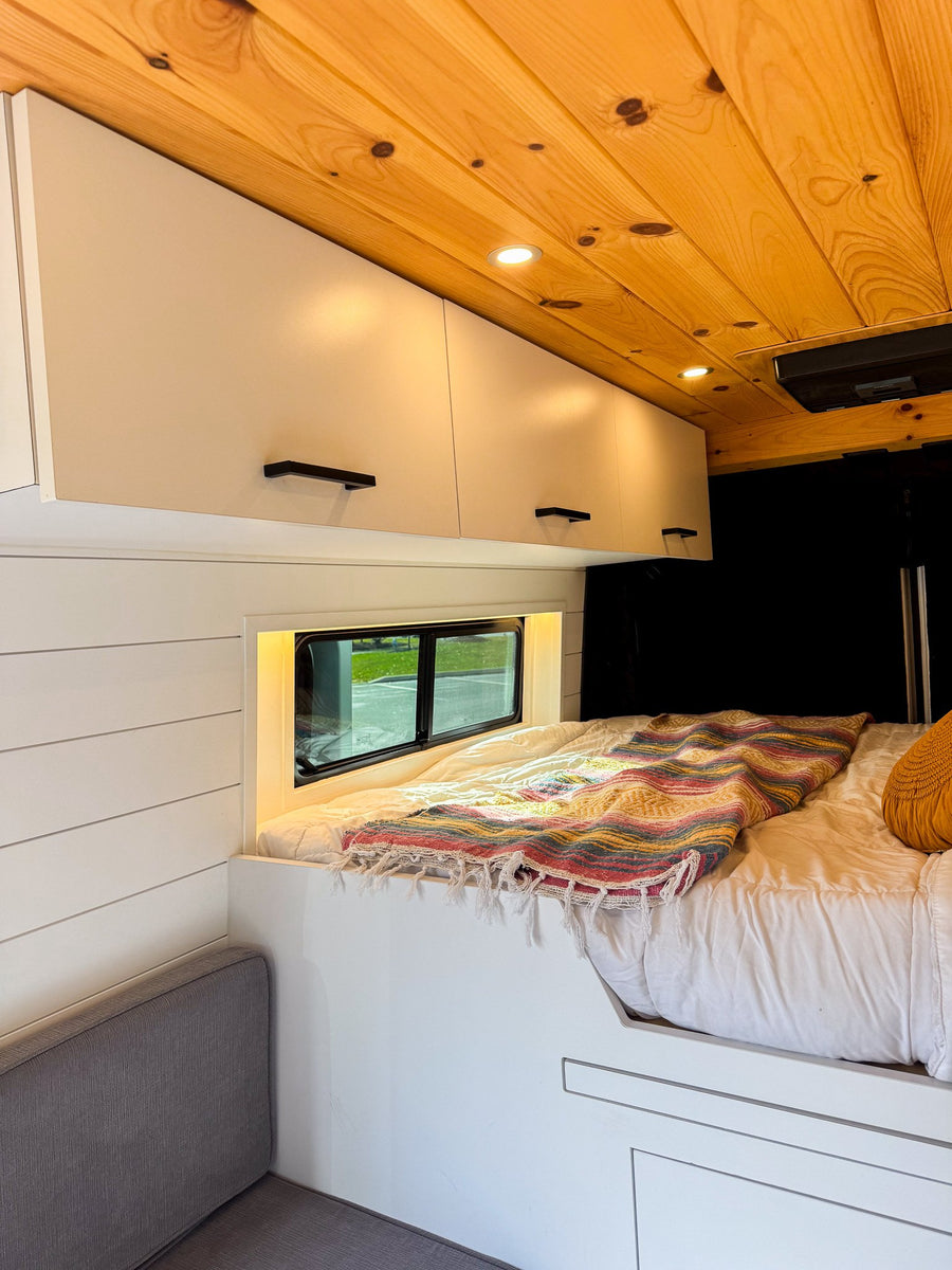parked on asphalt with trees & blue sky.|White RV rental van at a scenic waterfront park. A cargo ship sails past while joggers enjoy the sunset view.|Two people enjoy the scenic river view from their RV rental van