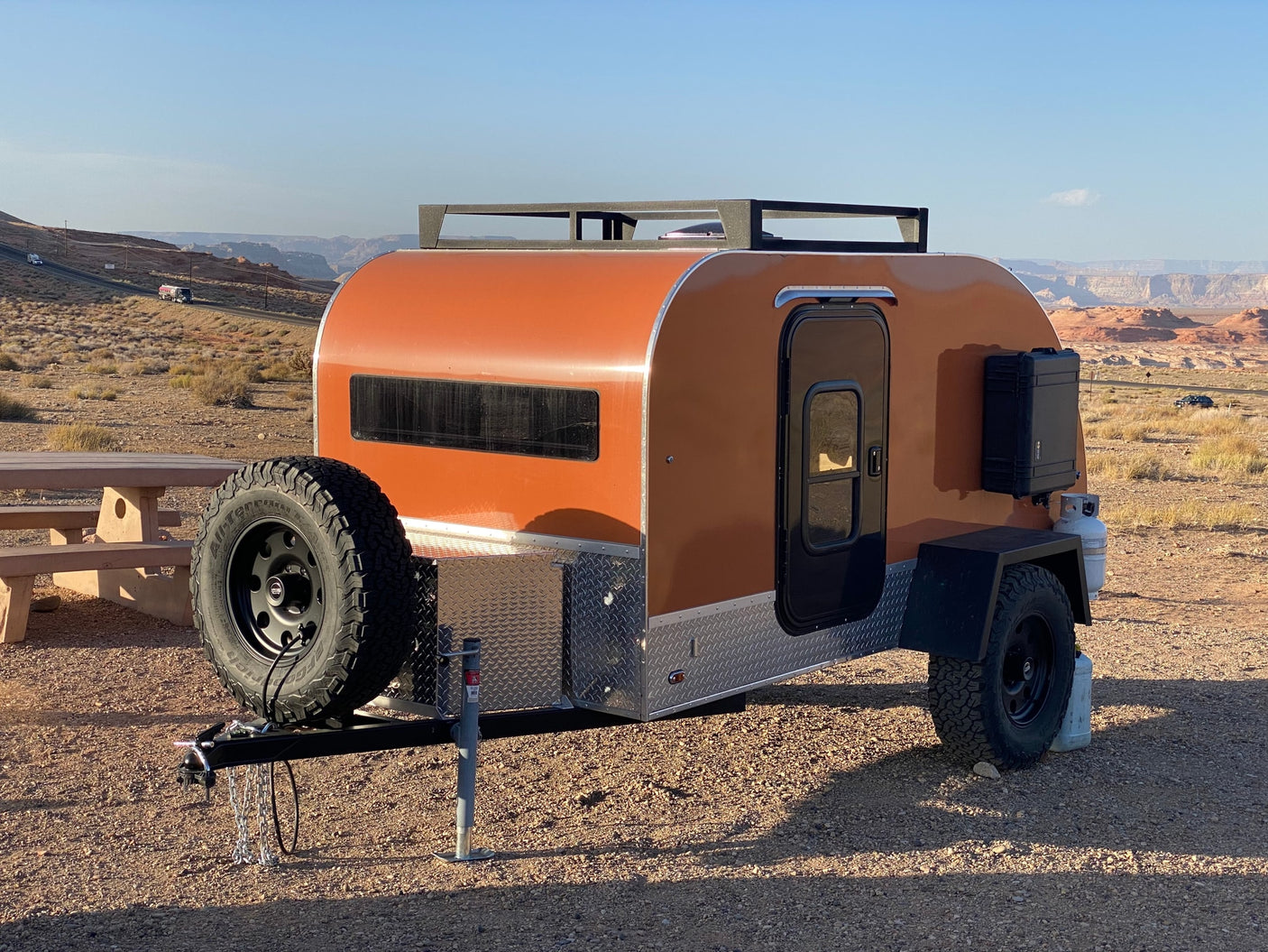 An orange teardrop RV rental parked in a vast desert landscape, ready for off-road travel.