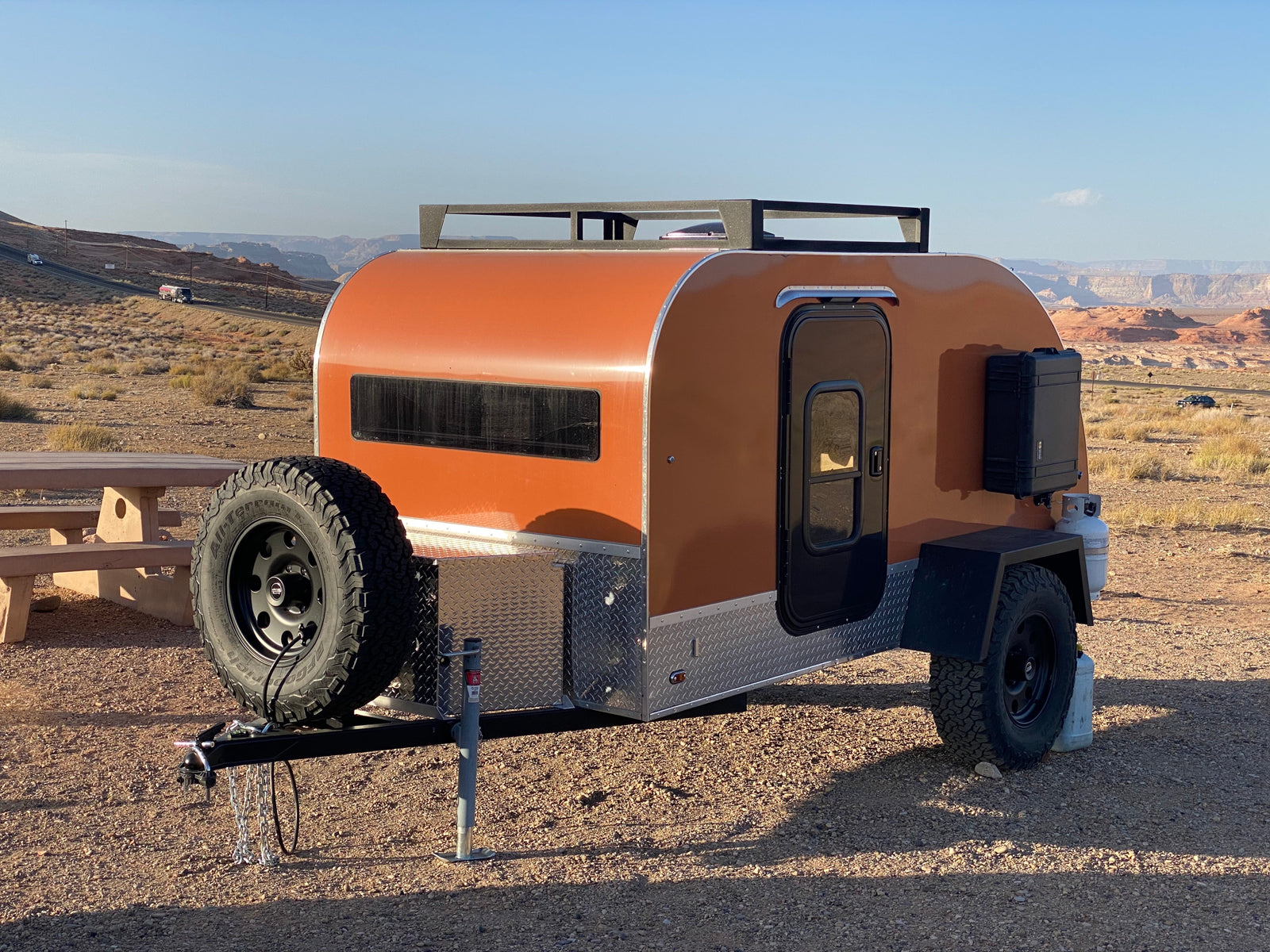 An orange teardrop RV rental parked in a vast desert landscape, ready for off-road travel.
