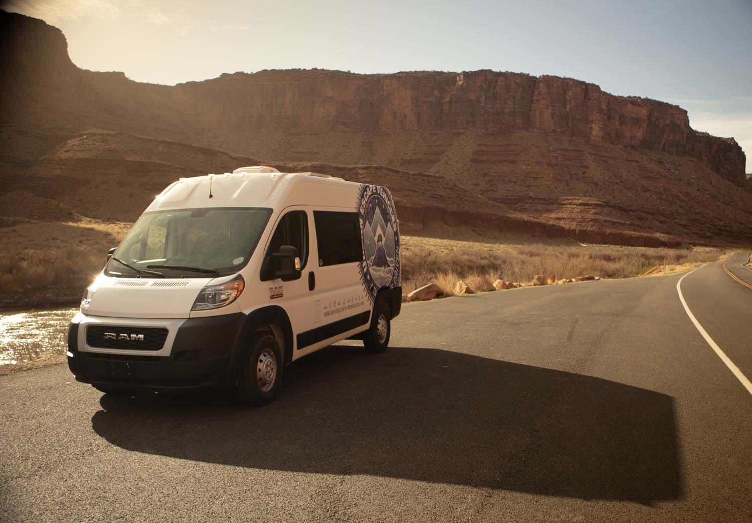 White **rv rental** camper van on a desert road, bathed in warm light, surrounded by majestic red rock canyons and a river.