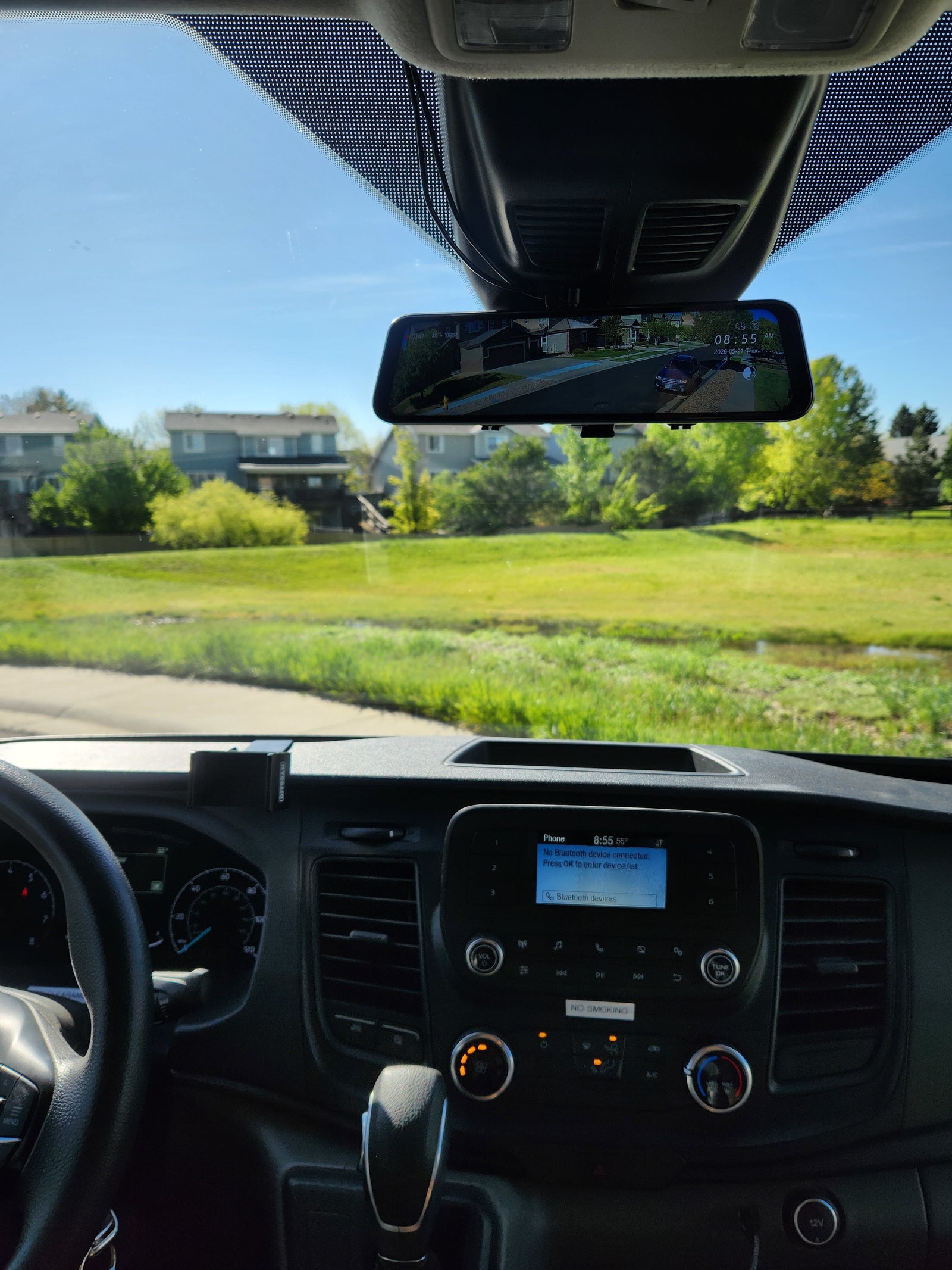 Driver's perspective inside an RV rental. View of dashboard, digital rearview mirror (showing street), and infotainment screen on a sunny day.