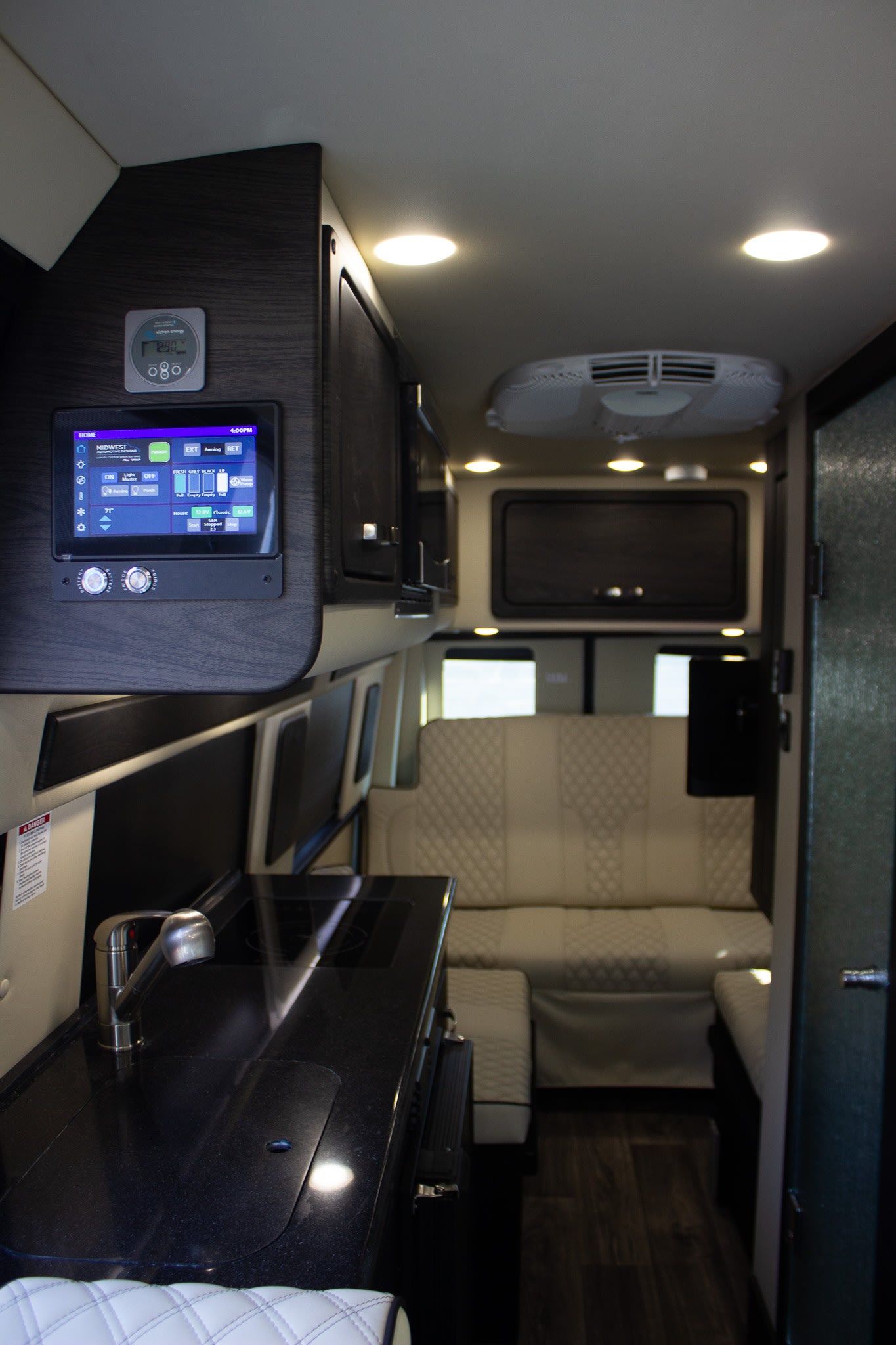 Modern rv rental interior with smart control panel, sleek kitchen, and plush quilted rear seating.