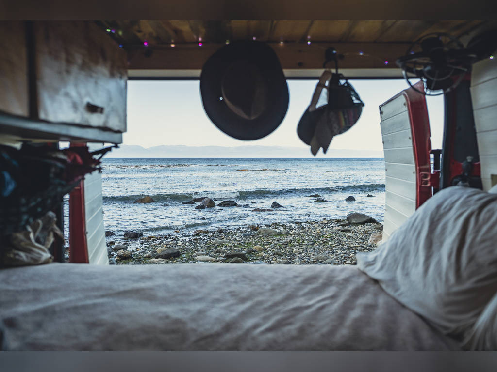 and bed. Perfect mobile living.|RV rental interior: A gear-filled tactical seat organizer hangs on a swiveled seat; a complex seat base optimizes space.|View from inside an RV rental shows a bed in foreground