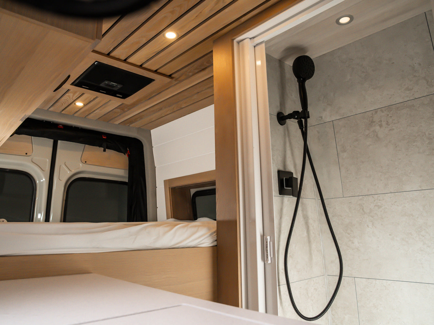 Enjoy a modern RV rental featuring a comfortable bed, beautiful wooden ceiling, and a compact, stylish shower area.