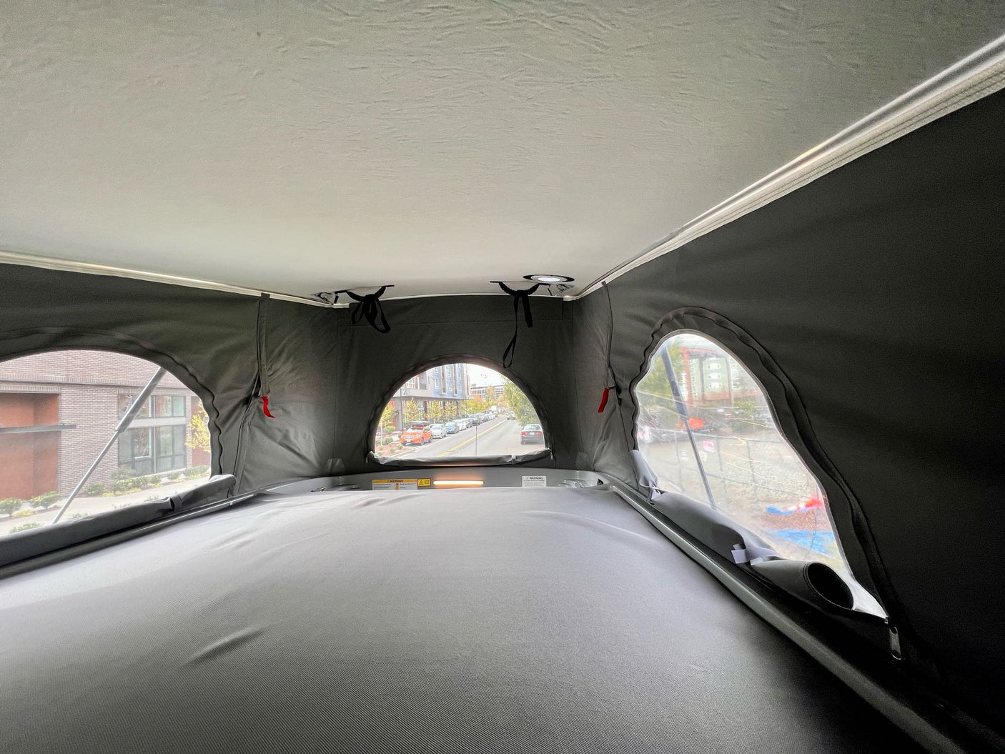 Inside an rv rental pop-top camper: light gray bed, fabric ceiling, and round windows offering street views.
