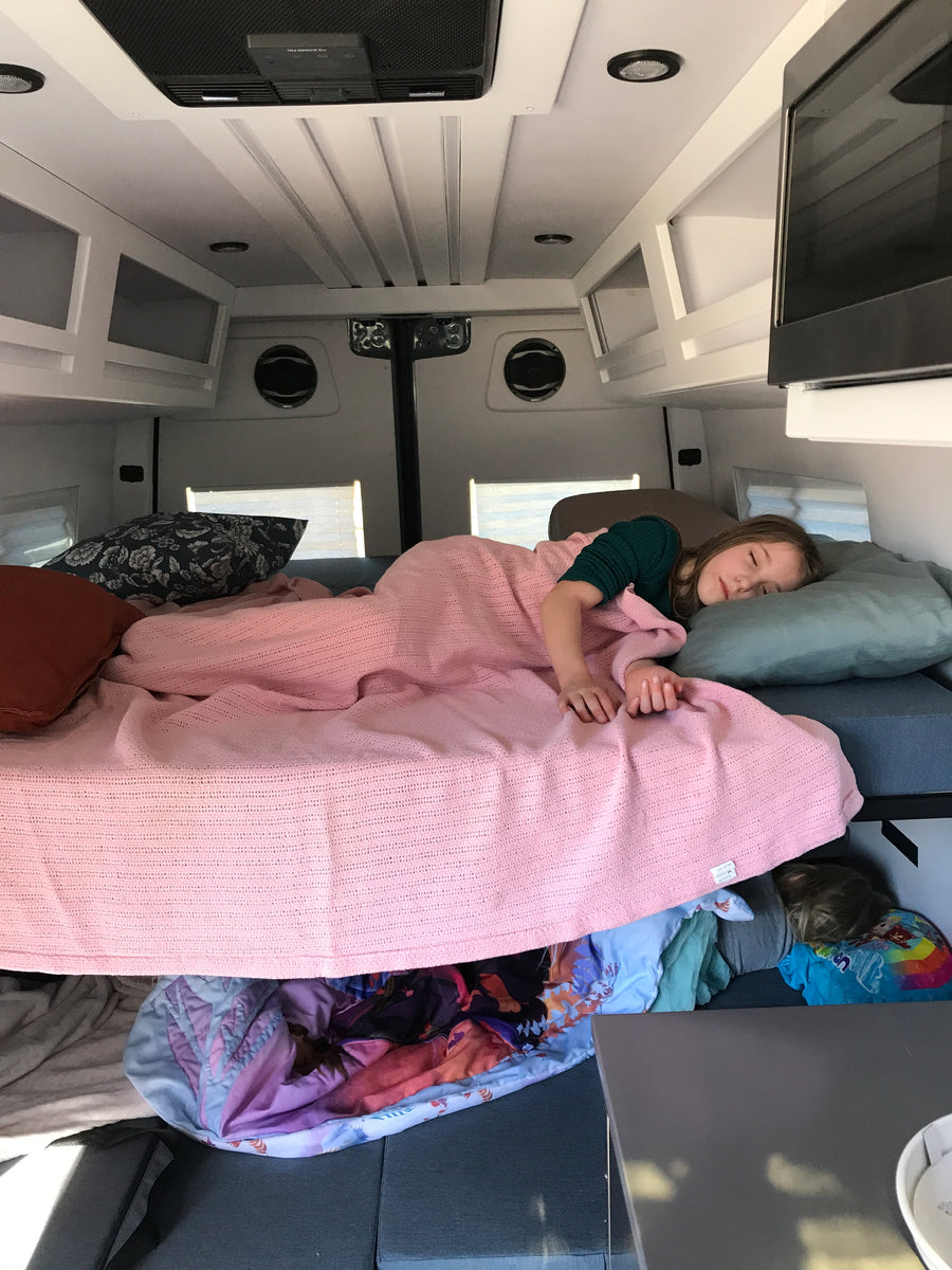 Peaceful sleep in an rv rental: child on bed, another below. Cozy travel van interior with overhead storage.