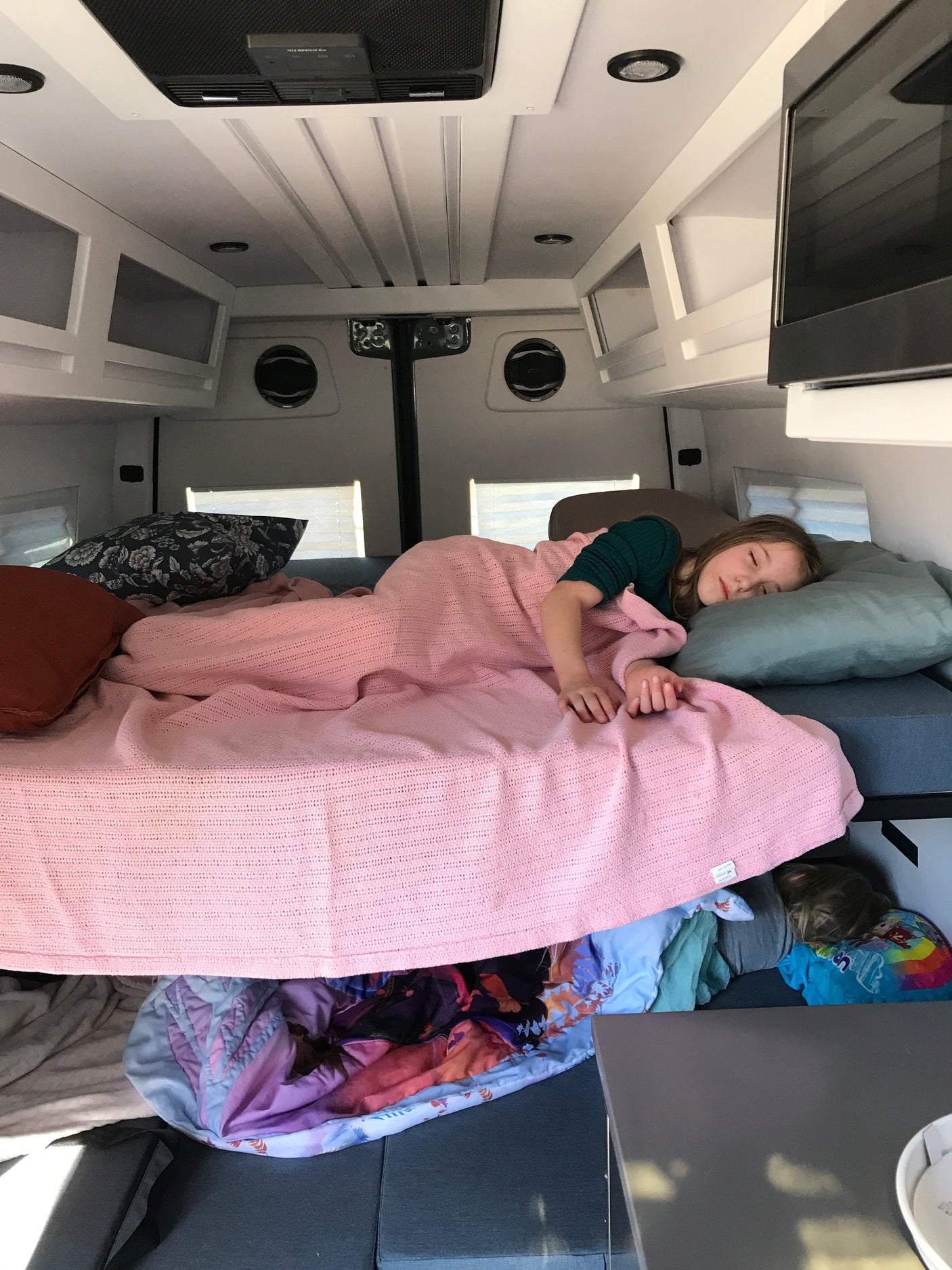 Peaceful sleep in an rv rental: child on bed, another below. Cozy travel van interior with overhead storage.