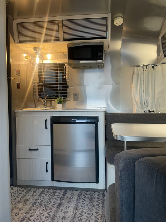 Cozy RV rental interior with a compact kitchen including a Dometic fridge, microwave, and a comfortable dining lounge.