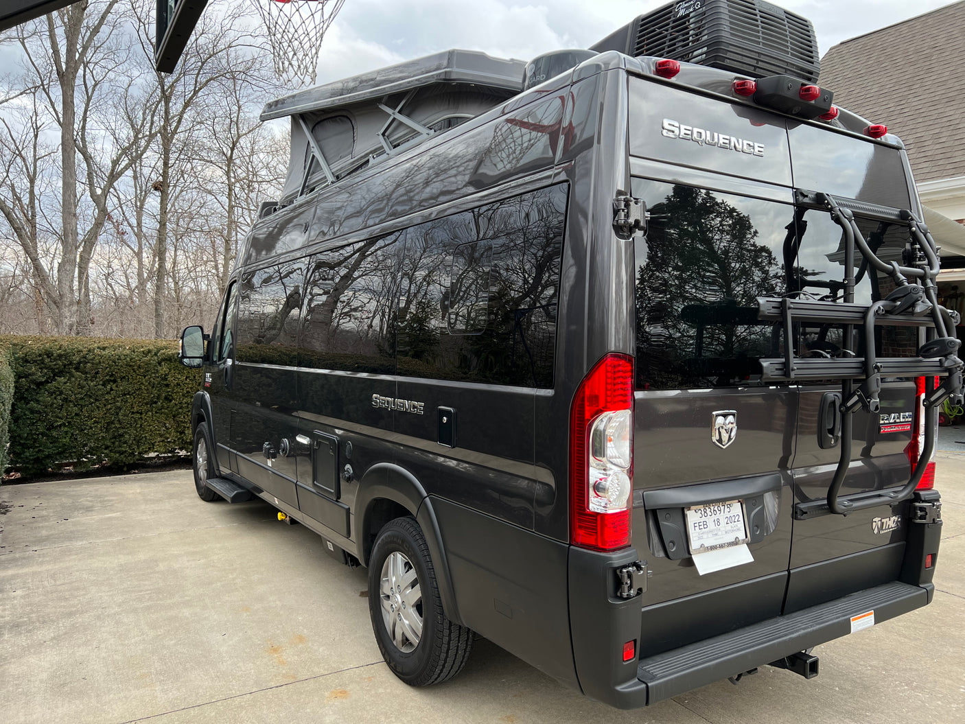 Dark gray Thor Sequence camper van RV rental, with a pop-top and rear bike rack, parked on a driveway.