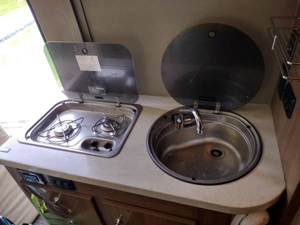 is parked with a cooler on a rear cargo carrier.|Compact RV rental interior: kitchen sink