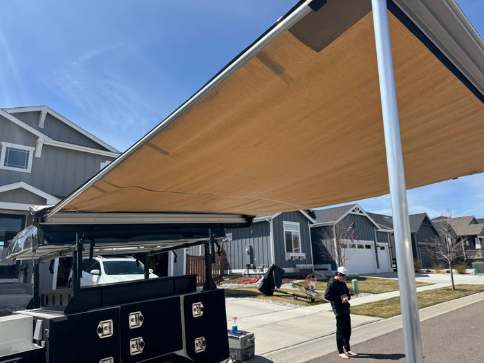 Extended awning from an RV rental, an off-road camper trailer, in a residential area. A person stands nearby.