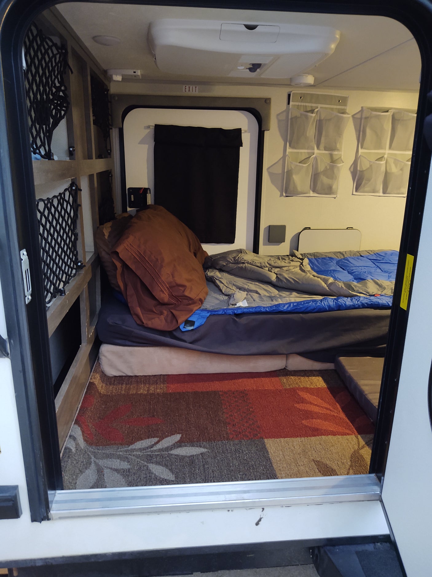 RV rental interior: bed, hanging organizers, and under-bed storage nets for compact living, viewed from the rear hatch.