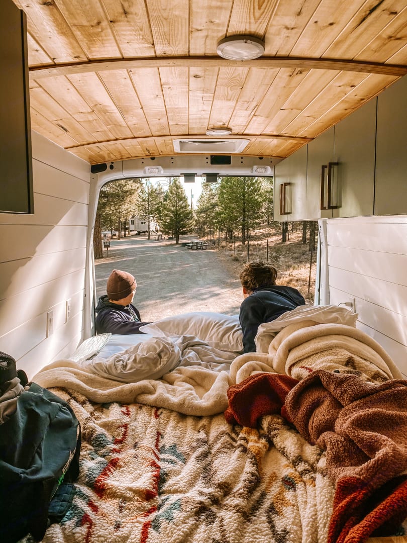and a white honeycomb tile backsplash.|Cozy rv rental interior: two people on a soft bed looking out at a tranquil — photo 3