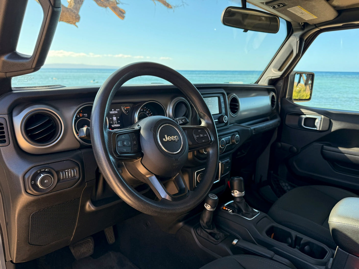 RV rental Jeep interior with ocean view. Dashboard details: 77°F, tire pressure. Ready for coastal adventure!