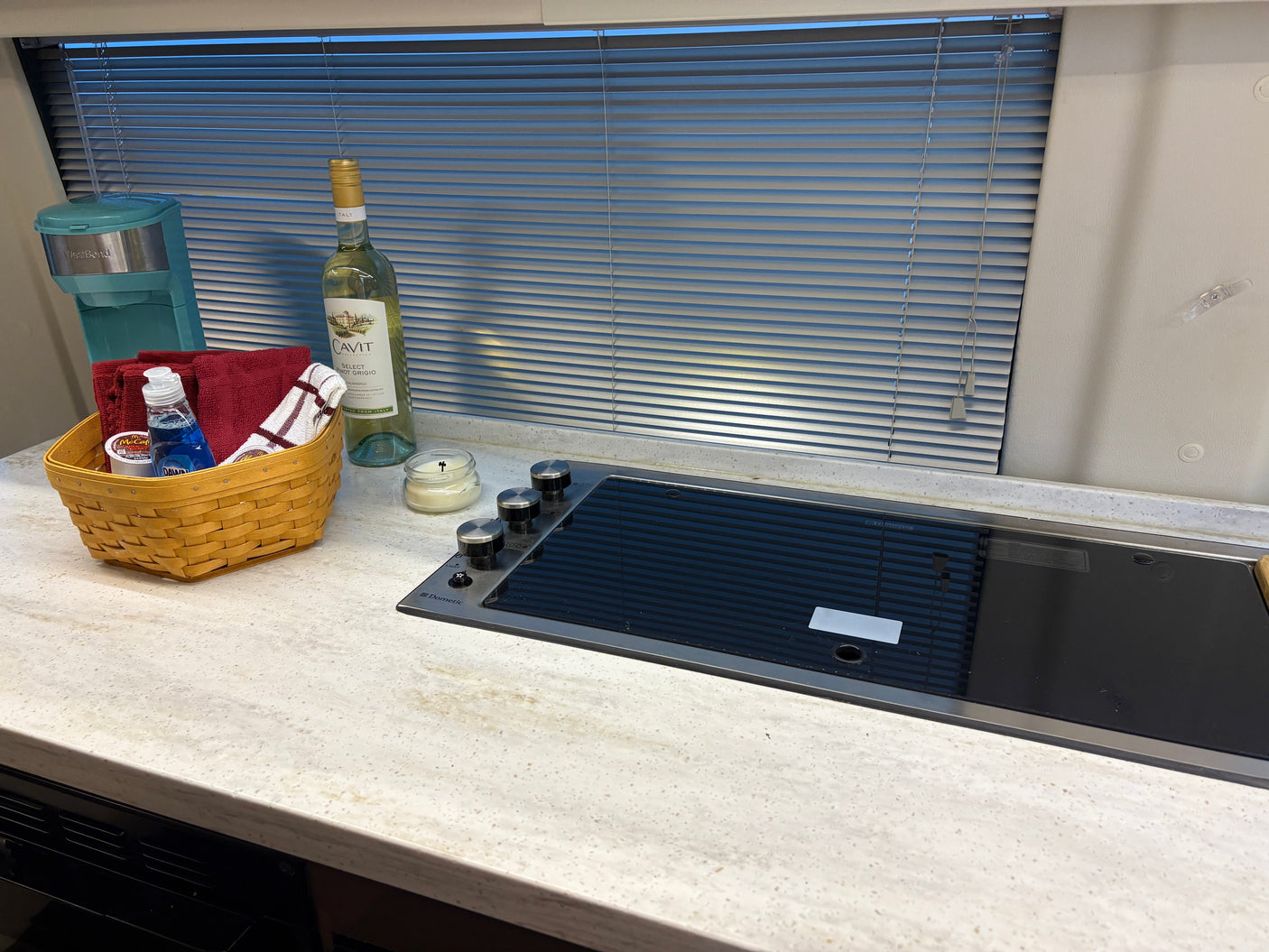 RV rental kitchen: a bright countertop with an induction cooktop, coffee maker, wine, and a basket holding towels & soap.