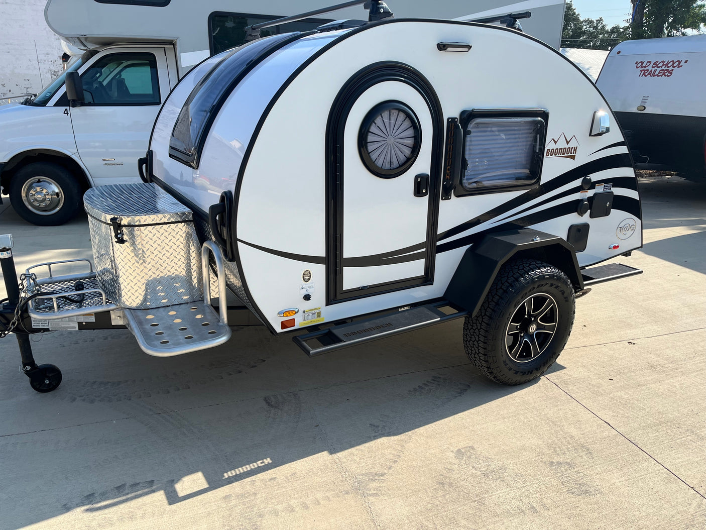 A white Boondock teardrop RV/camper, ideal for RV rental adventures, featuring off-road tires and a front storage box.