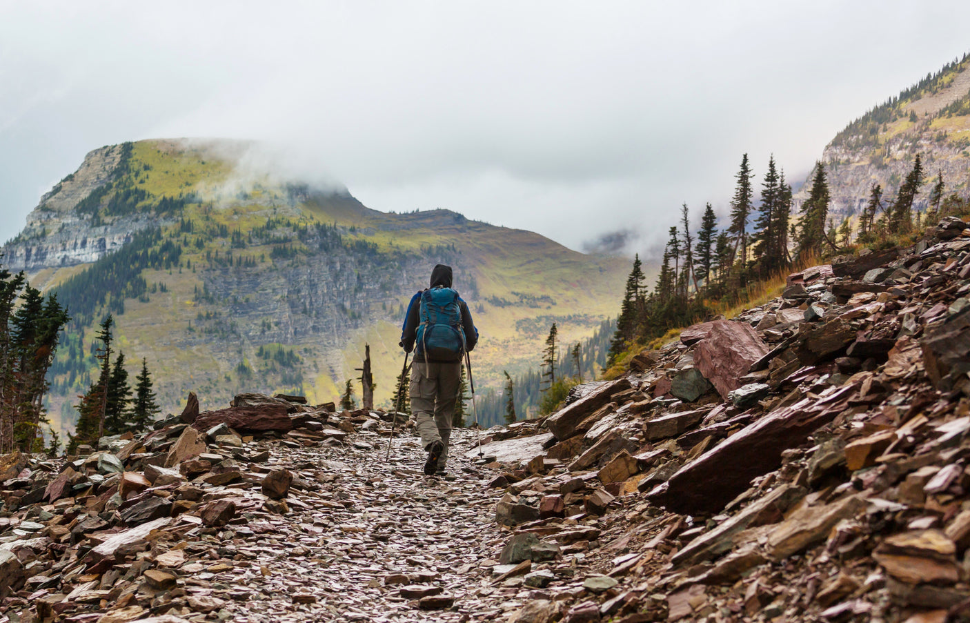 Hiker on a rugged, rocky mountain trail with misty peaks in the distance. An RV rental makes reaching these outdoor adventures easy.