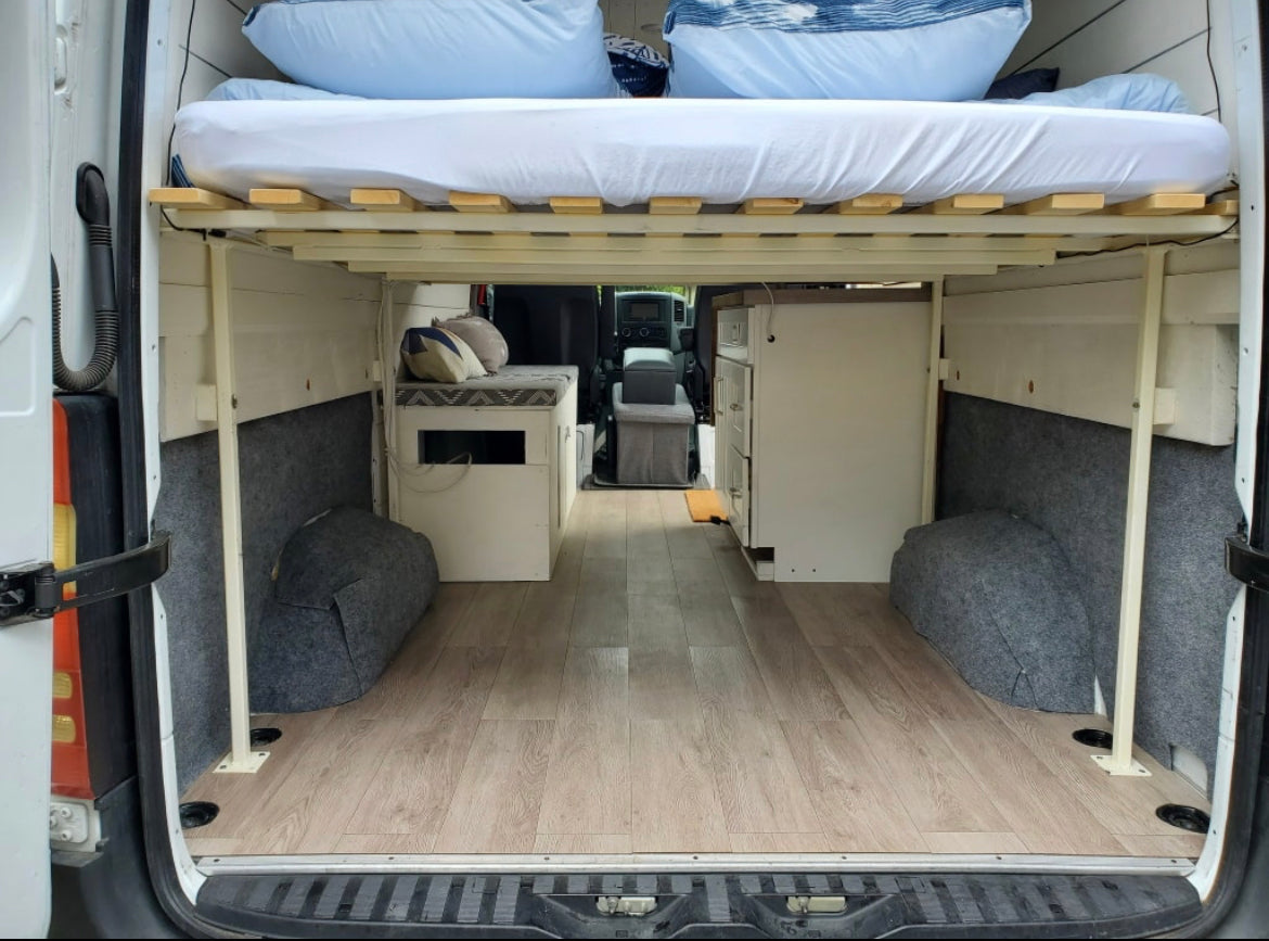 Spacious camper van interior, ideal for RV rental. Raised bed, under-bed storage, and compact kitchen offer comfortable mobile living.