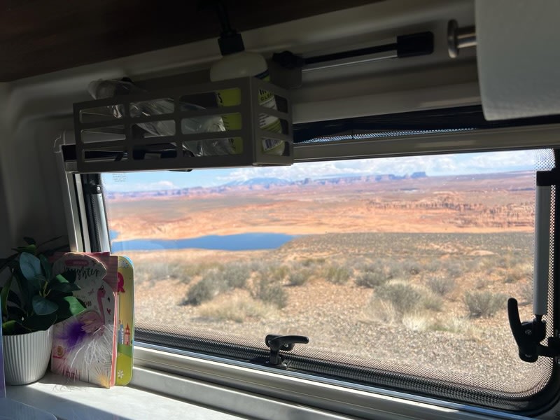 Enjoy the breathtaking desert and lake views from your RV rental. Inside: a cozy window setup with books and a plant.
