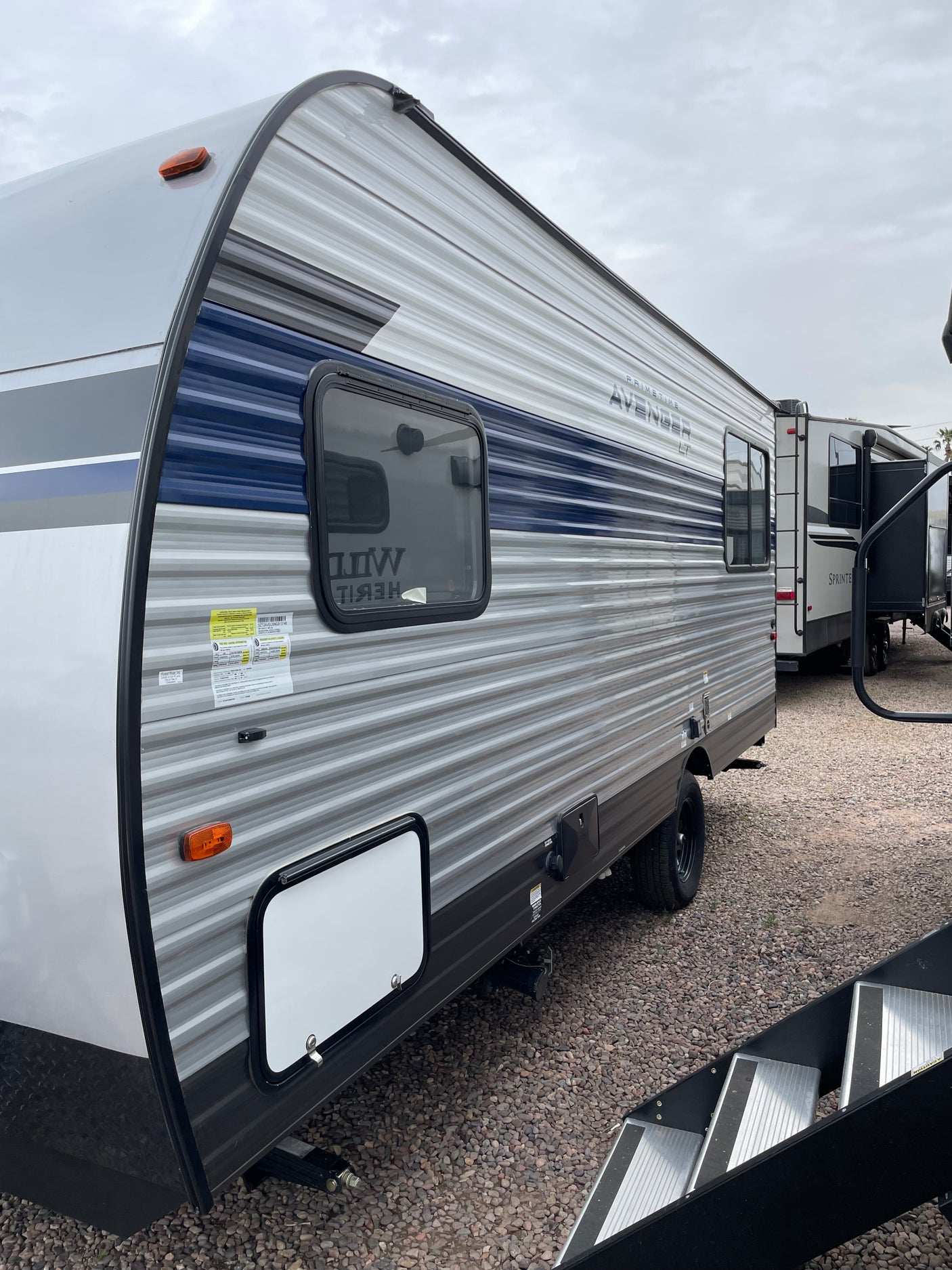 Spacious grey and blue travel trailer RV, perfect for your next RV rental adventure, parked on a gravel lot.