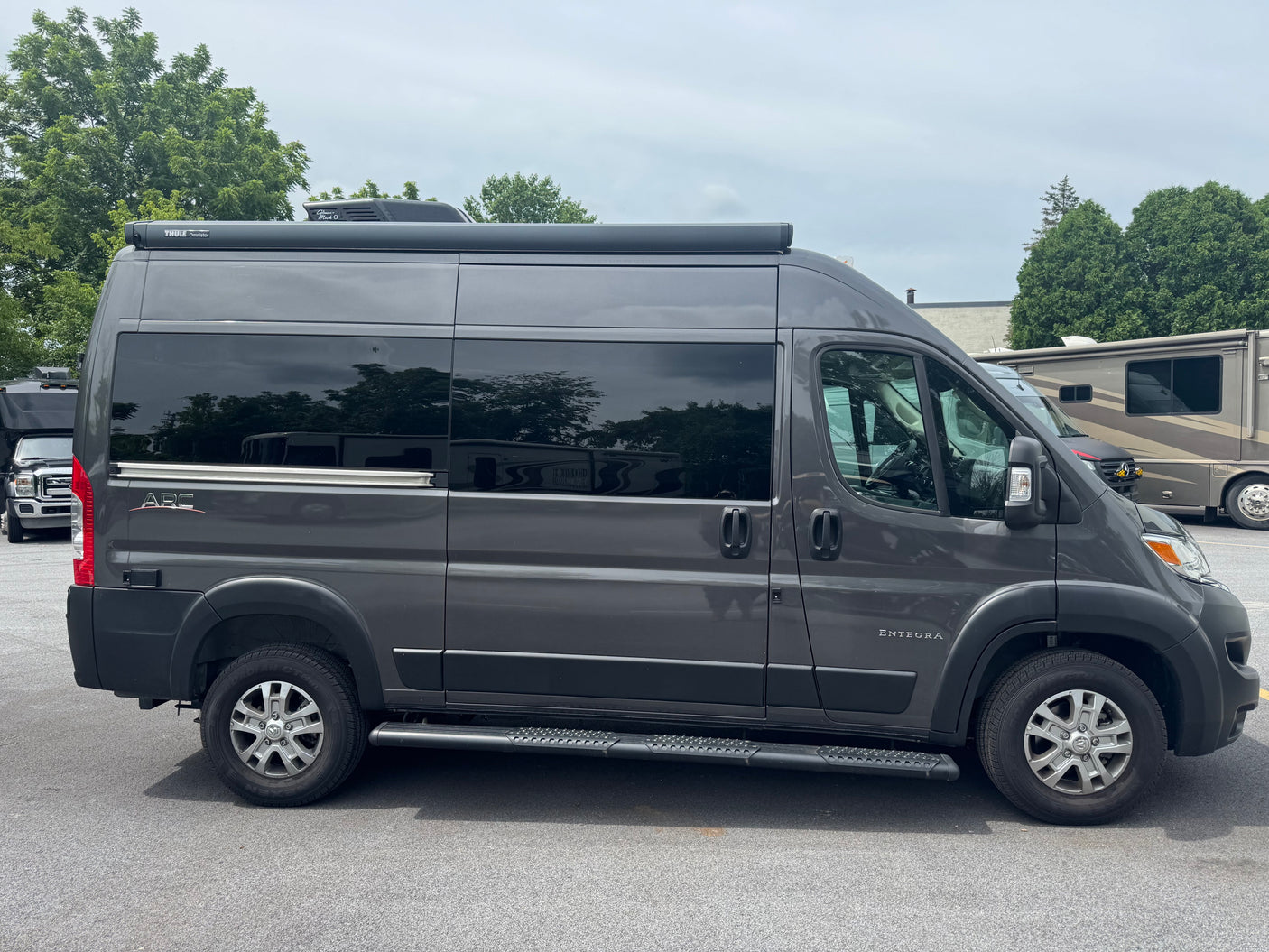 Dark grey Entegra ARC camper van, an RV rental, with a Thule awning and roof AC, parked on asphalt.