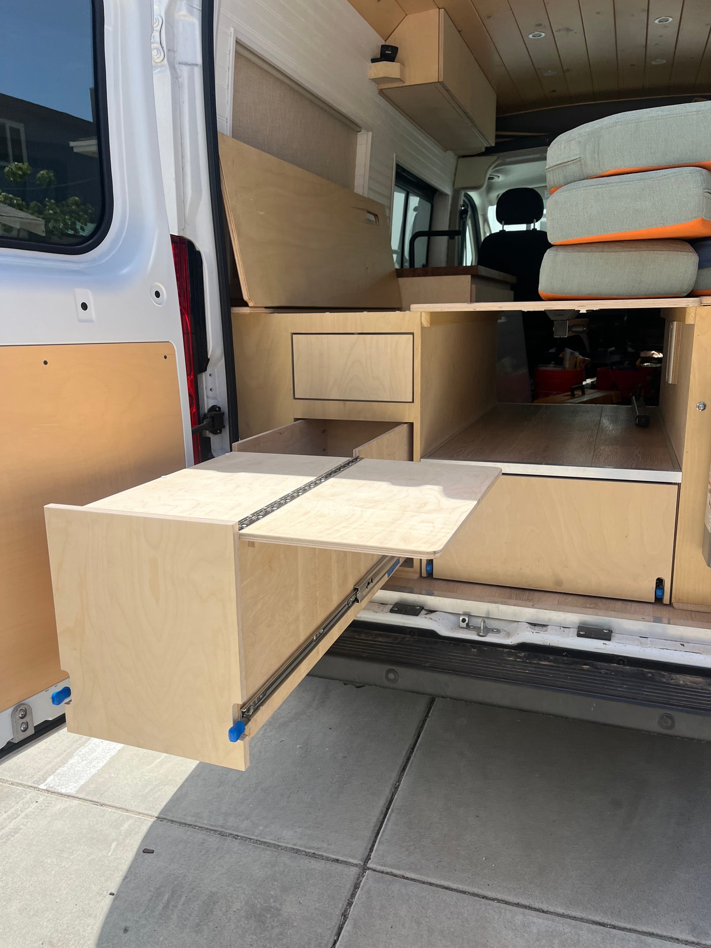 RV rental: Custom camper van interior with light wood cabinetry & large pull-out table/storage from the rear.